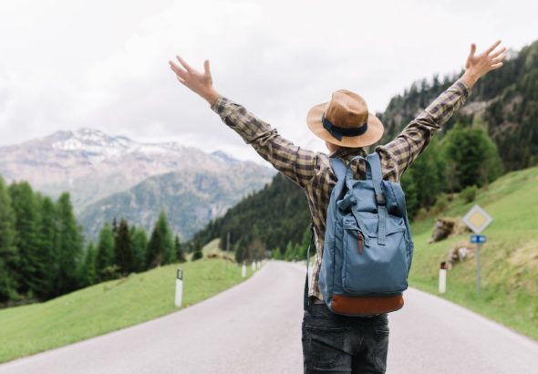 happy-male-traveler-posing-with-hands-up-standing-highway-looking-distant-trees